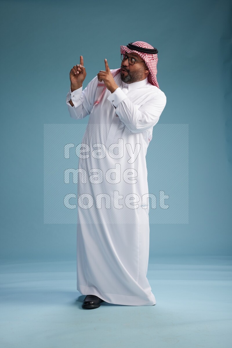Saudi Man with shimag Standing Interacting with the camera on blue background