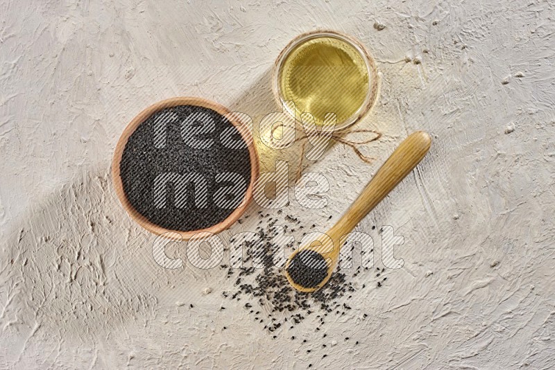 A wooden bowl and spoon full of black seeds and a glass jar of black seeds oil on a textured white flooring in different angles