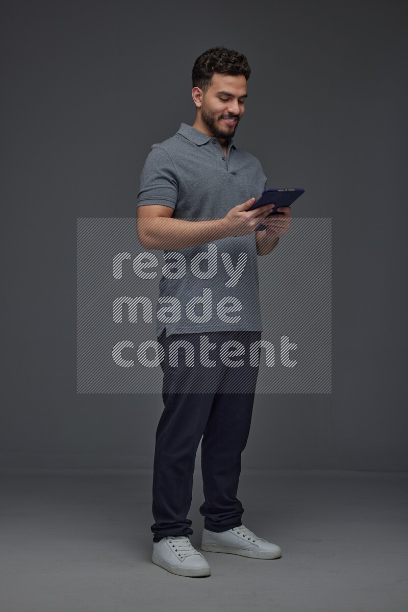 A man wearing casual standing and using his tablet and making multi hand gestures different angles eye level on a gray background