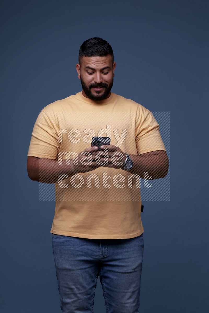 A man Texting on his phone on Blue Background wearing Orange T-shirt