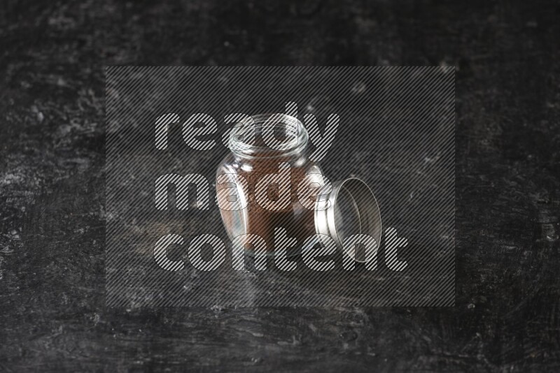 وعاء بهارات زجاجي ممتلئ ببودرة القرنفل على أرضية سوداء