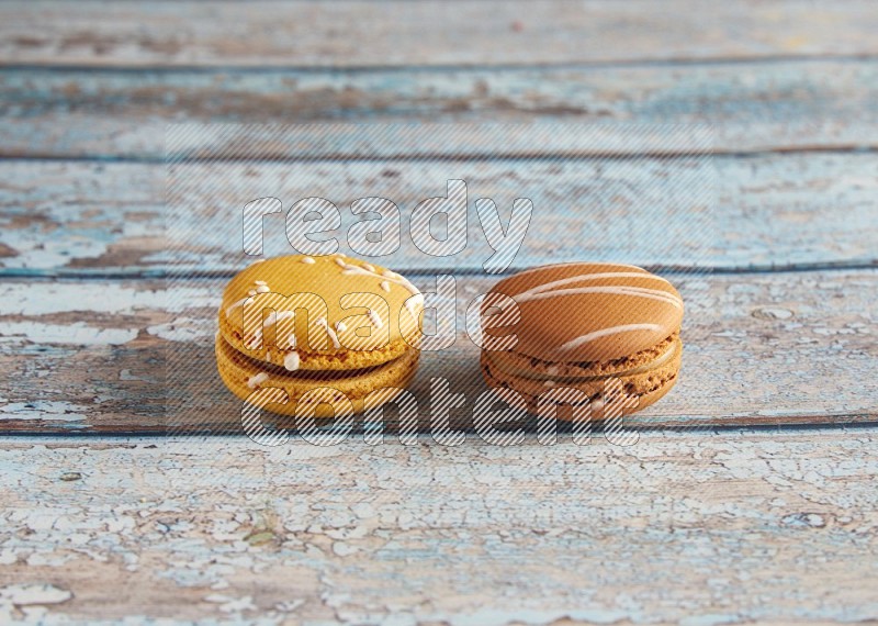 45º Shot of of two assorted Brown Irish Cream, and Yellow Piña Colada macarons on light blue background