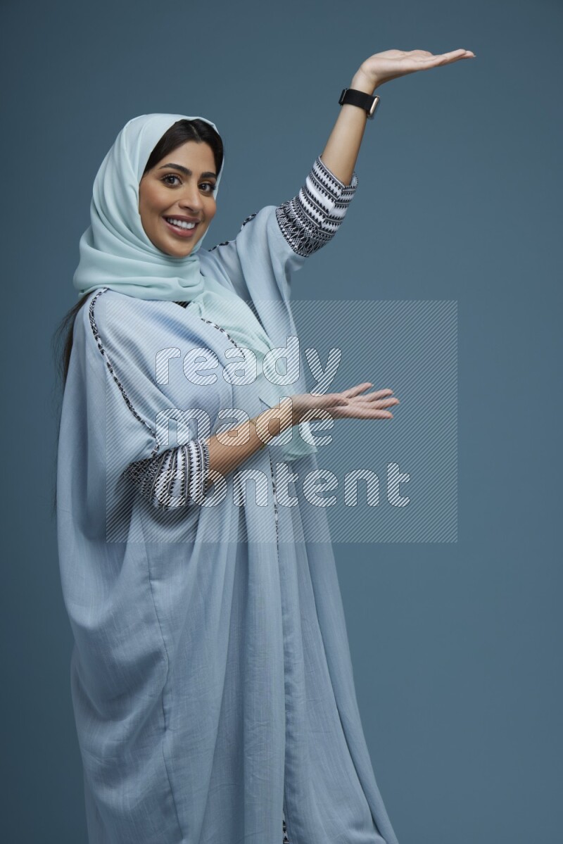 A Saudi woman pointing in a blue background wearing a Blue abaya