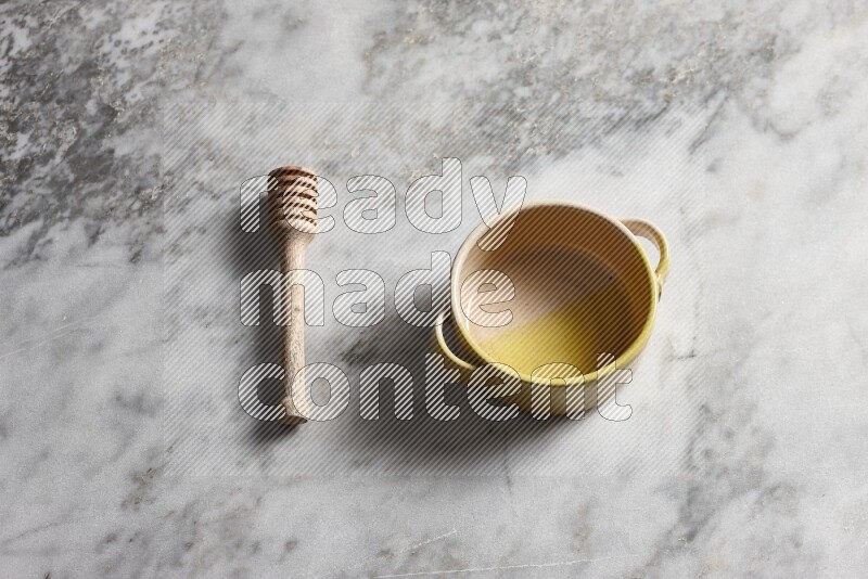 Multicolored pottery bowl with wooden honey dipper on the side on grey marble background