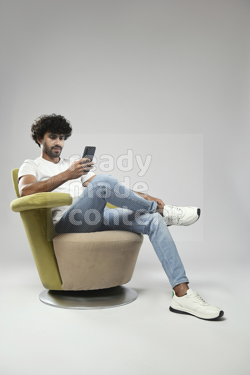 A man wearing casual sitting on a chair browsing on the phone on white background
