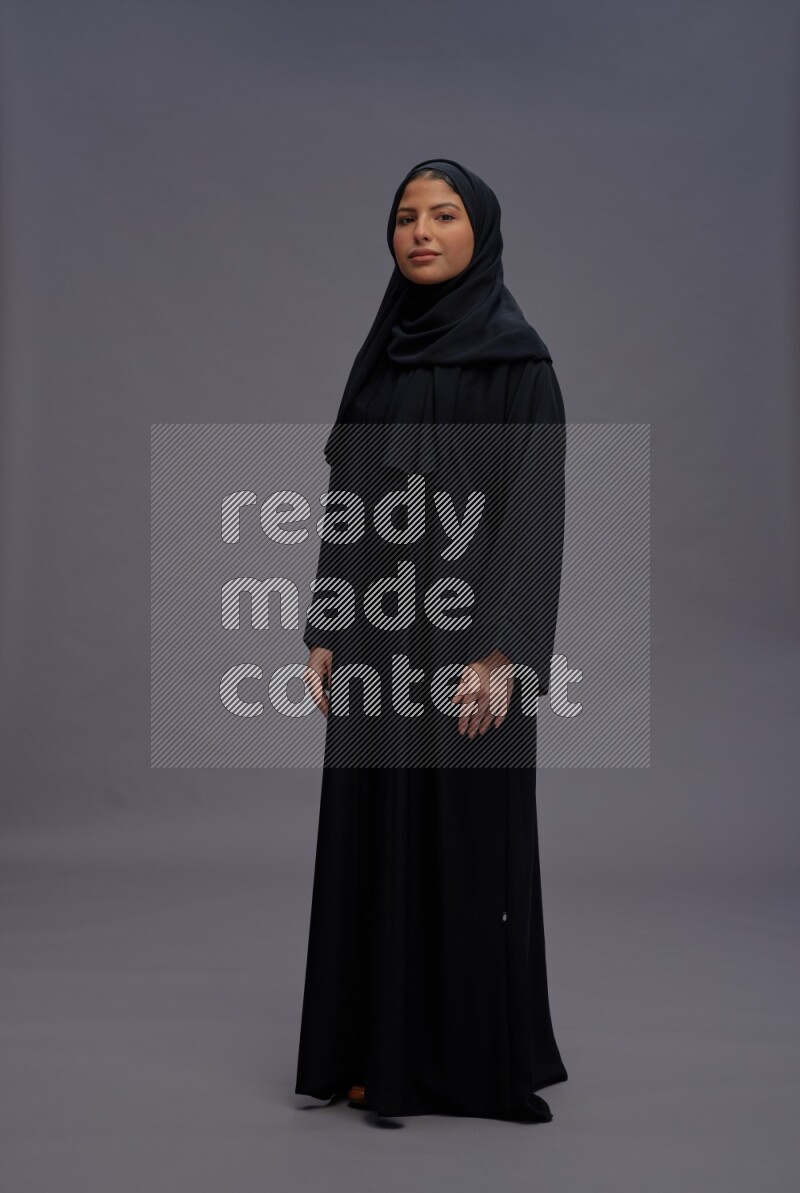 Saudi woman wearing Abaya standing interacting with the camera on gray background