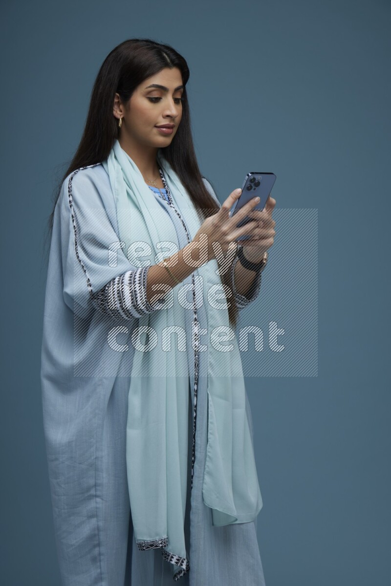 A Saudi woman Texting in a blue background wearing blue Abaya with no hijab