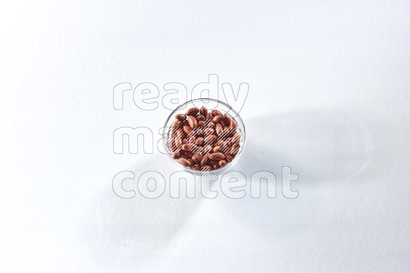A glass bowl full of red skin peanuts on a white background in different angles