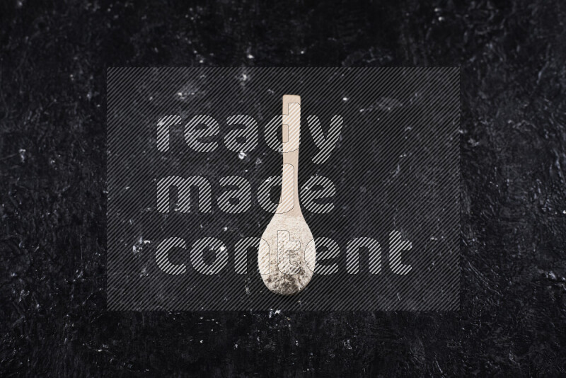 A wooden spoon full of onion powder on black background