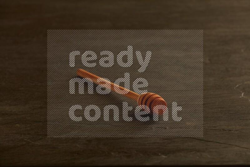 Wooden honey dipper on black slate background