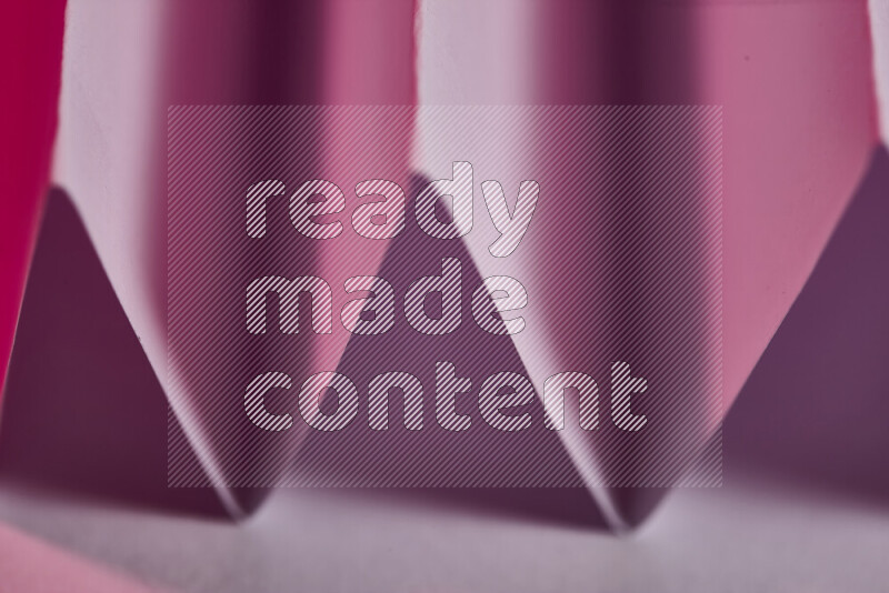 A close-up abstract image showing sharp geometric paper folds in pink gradients