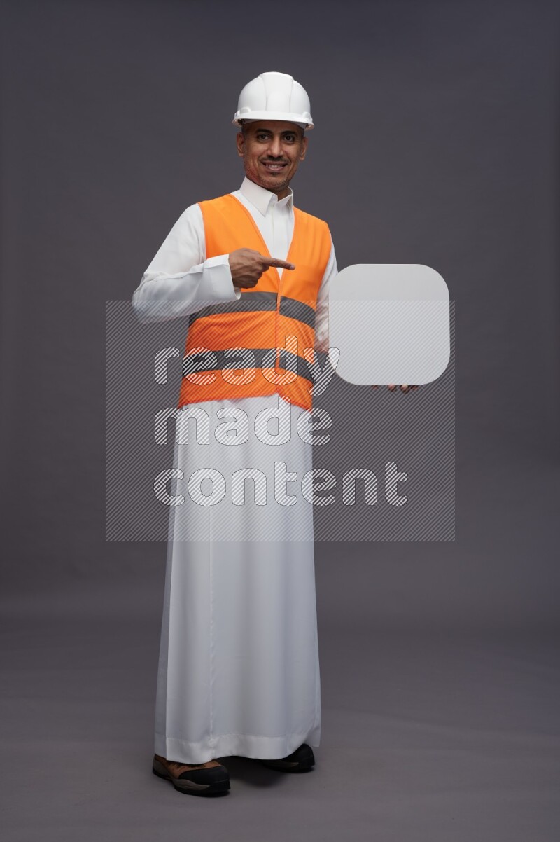 Saudi man wearing thob with engineer vest standing holding social media sign on gray background