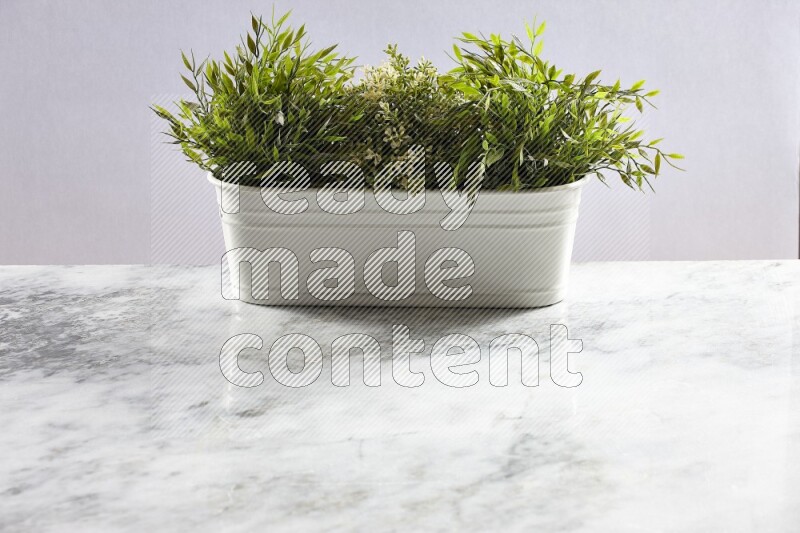 Multiple green artificial plants in white pot on grey marble background