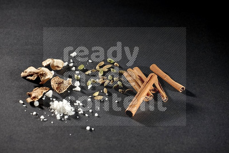 Ginger, salt, cardamom and cinnamon sticks on black flooring