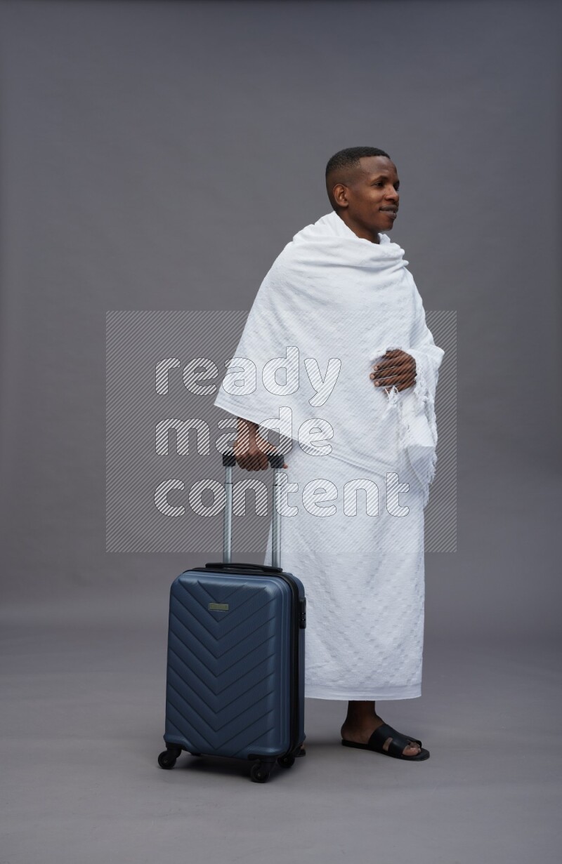 A man wearing Ehram Standing holding traveling bag on gray background
