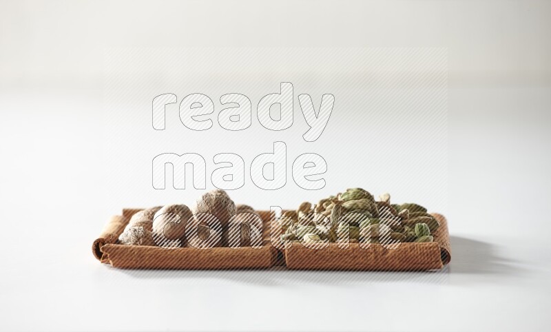 مربعان من أعواد القرفة ممتلئان بحبوب الهيل وجوزة الطيب علي خلفية بيضاء