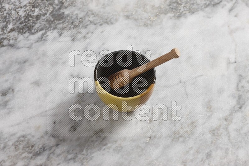 Multicolored pottery bowl with wooden honey dipper in it on grey marble background