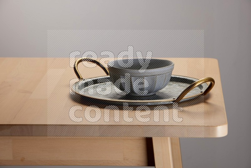 grey bowl placed on a rounded stainless steel tray with golden handels on the edge of wooden table