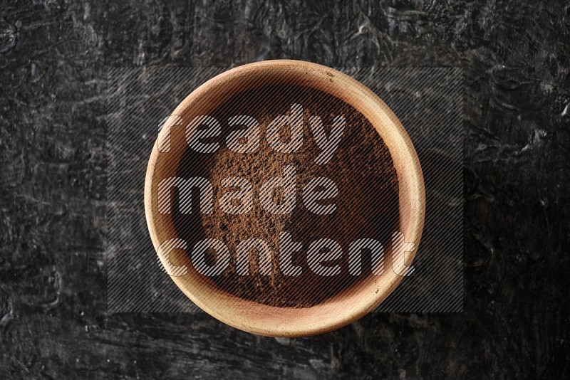 A wooden bowl full of cloves powder on a textured black flooring