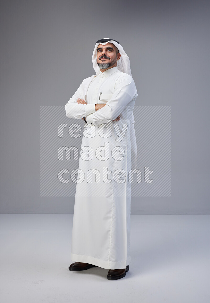 Saudi man Wearing Thob and white Shomag standing with crossed arms on Gray background