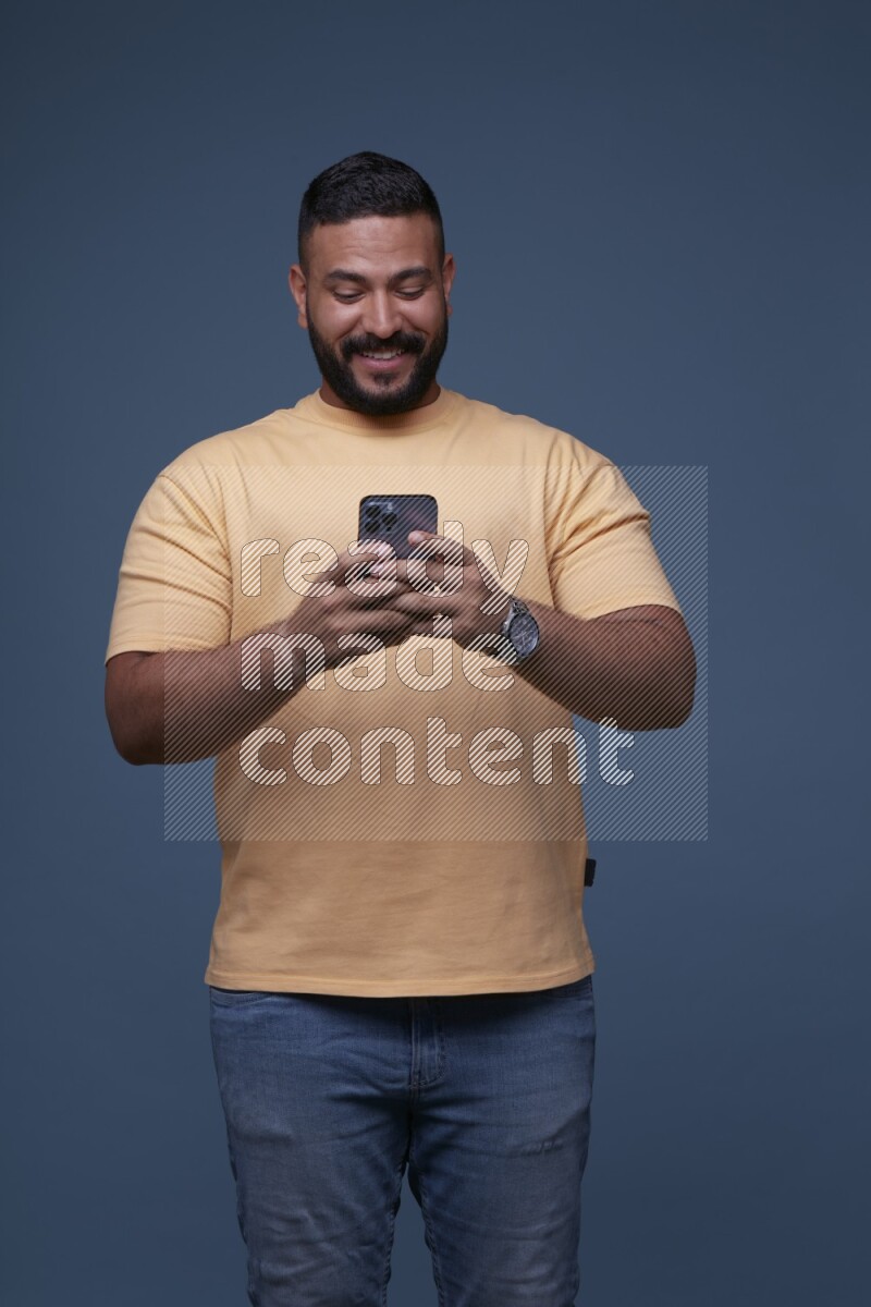 A man Texting on his phone on Blue Background wearing Orange T-shirt