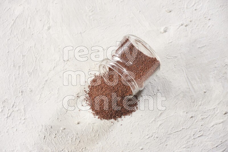 A glass jar full of garden cress seeds and jar is flipped and seeds are spread on a textured white flooring