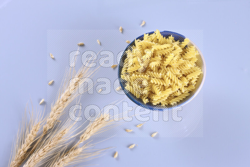 Raw pasta with wheat stalks on light blue background