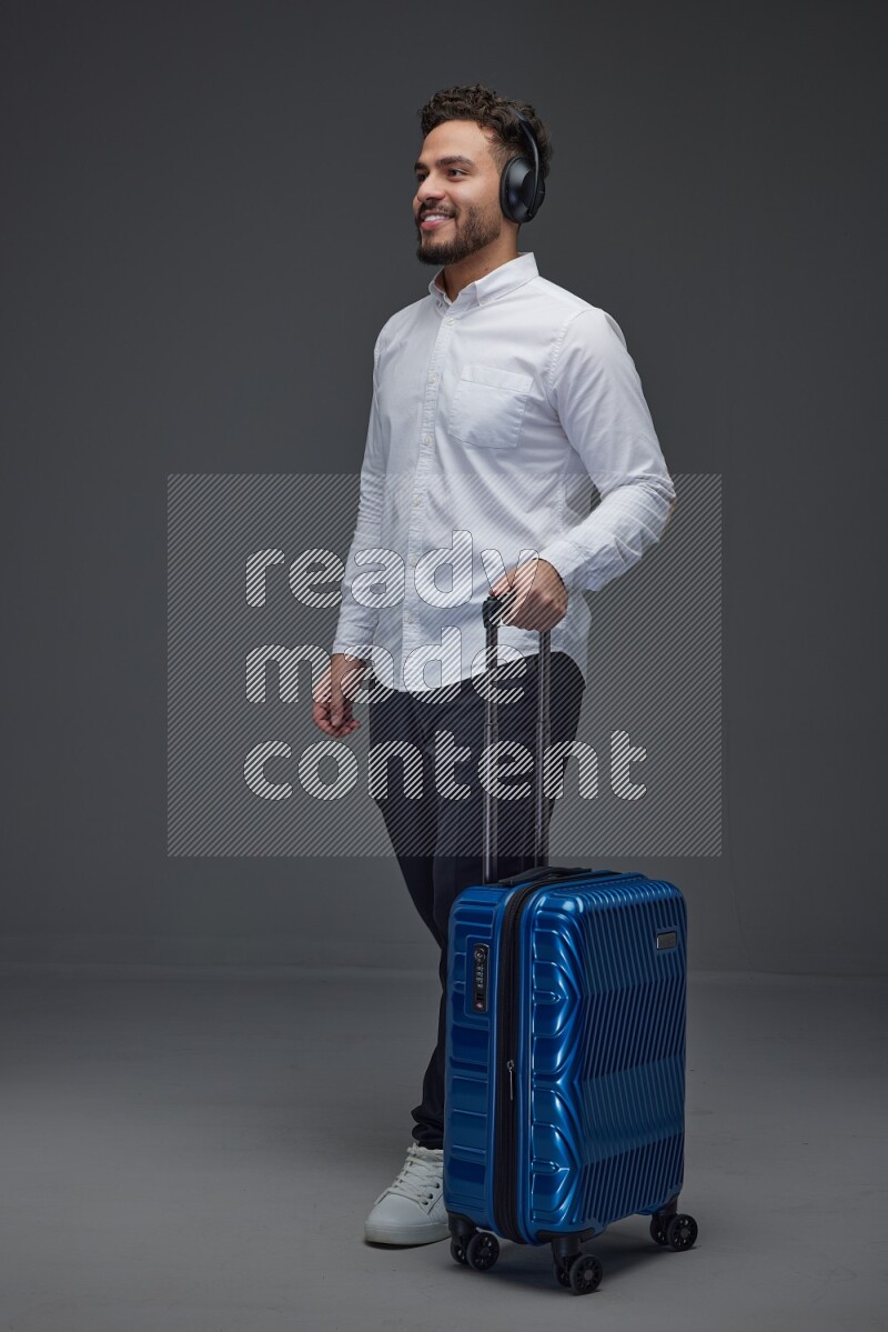 A man Posing with a carry-on with headsets  Wearing a White shirt on a grey background