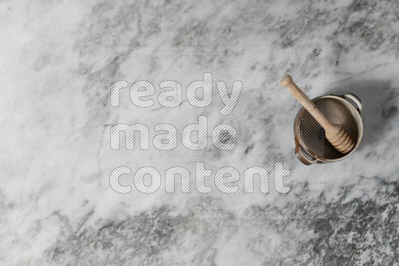 Multicolored pottery bowl with wooden honey dipper in it on grey marble background
