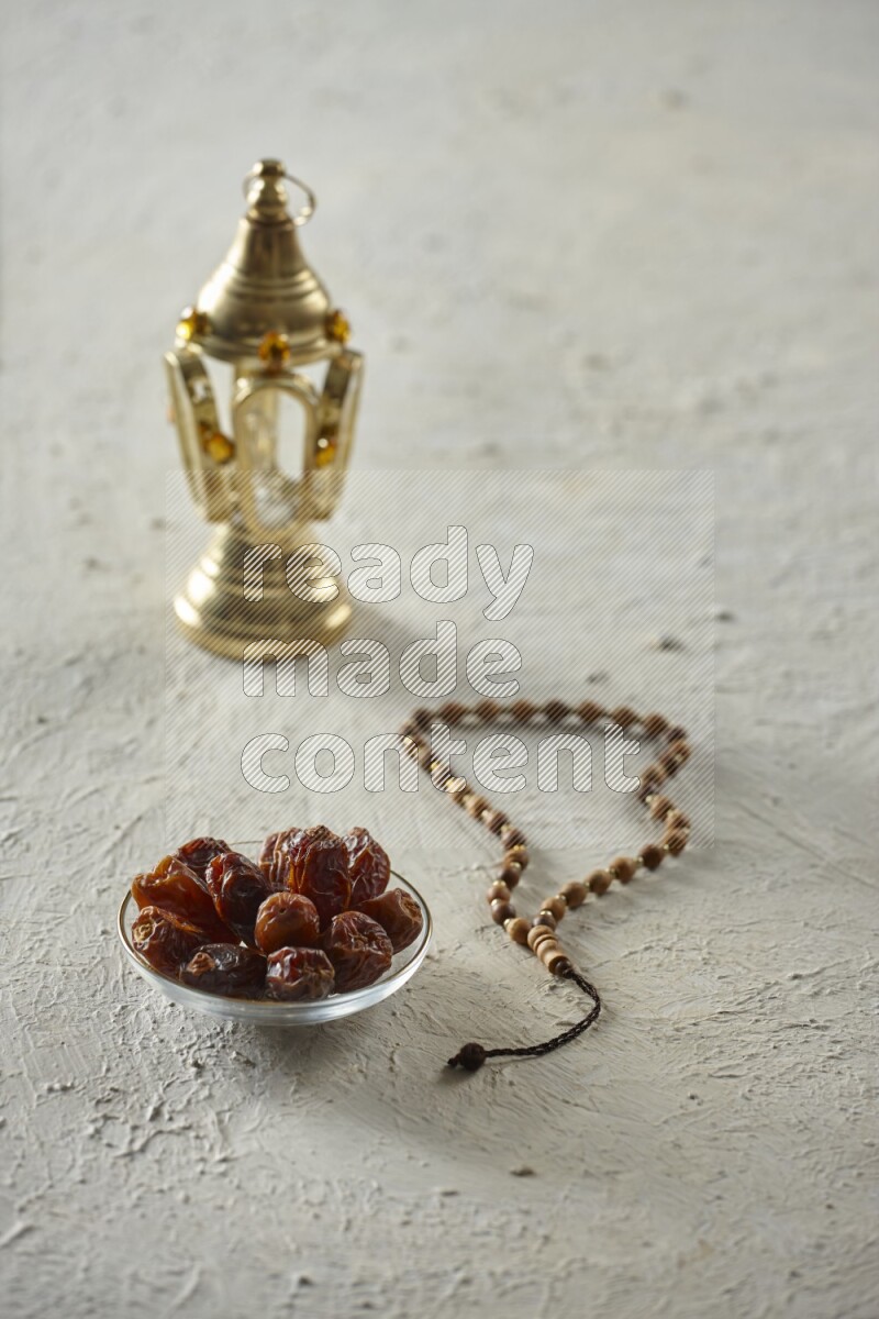 A golden lantern with different drinks, dates, nuts, prayer beads and quran on textured white background