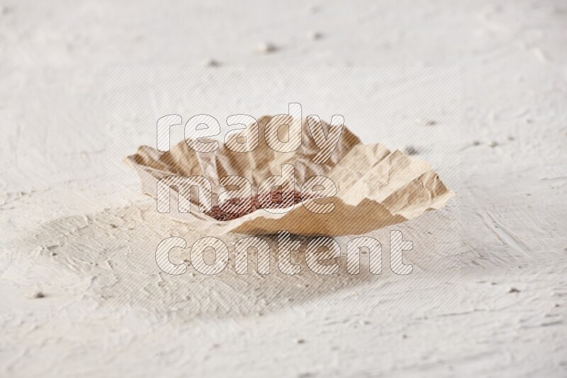A crumpled piece of paper full of garden cress seeds on a textured white flooring