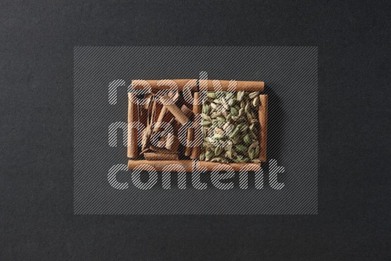 مربعان من أعواد القرفة ممتلئان بحبوب الهيل والقرفة علي خلفية سوداء