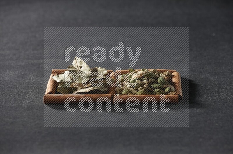 مربعان من أعواد القرفة ممتلئان بحبوب الهيل وأوراق الغار علي خلفية سوداء