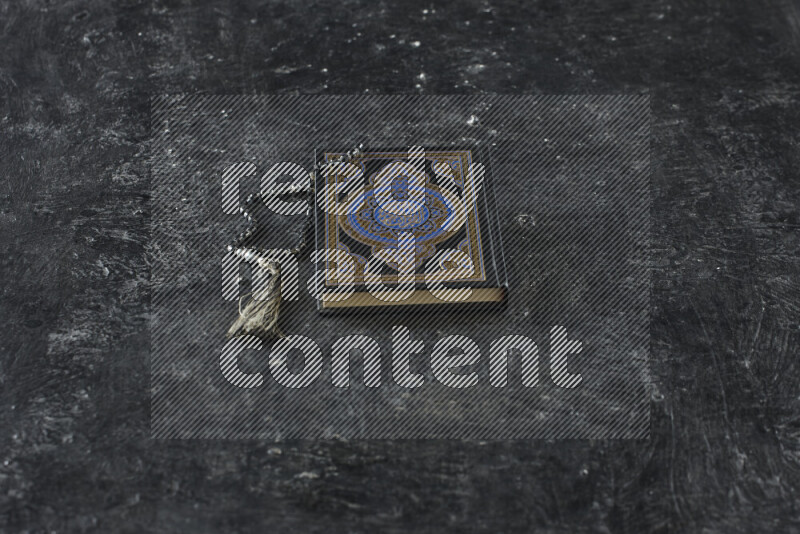 Quran with a prayer beads on textured black background