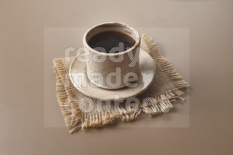 A beige pottery cup of coffee surrounded by roasted coffee beans on beige background