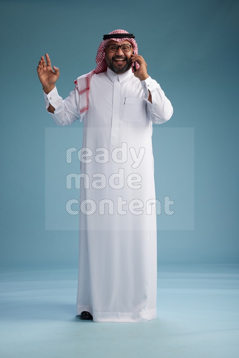 Saudi Man with shimag Standing talking on phone on blue background