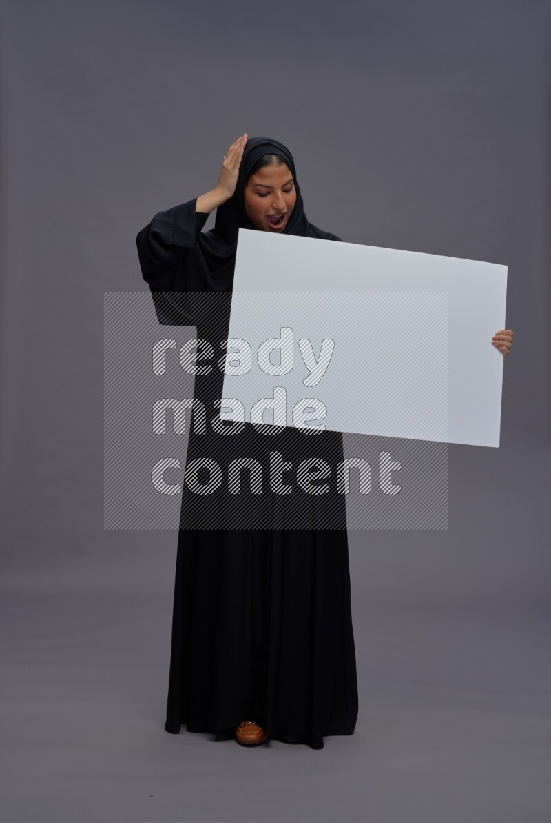 Saudi woman wearing Abaya standing holding white board on gray background