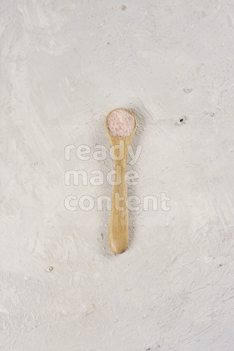 A wooden spoon full of pink himalayan salt on white background