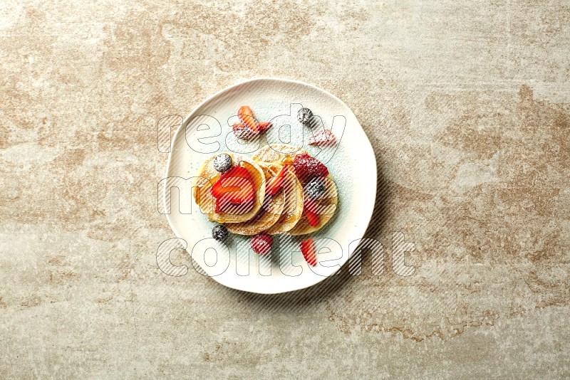 Five stacked mixed berries mini pancakes in a bicolor plate on beige background