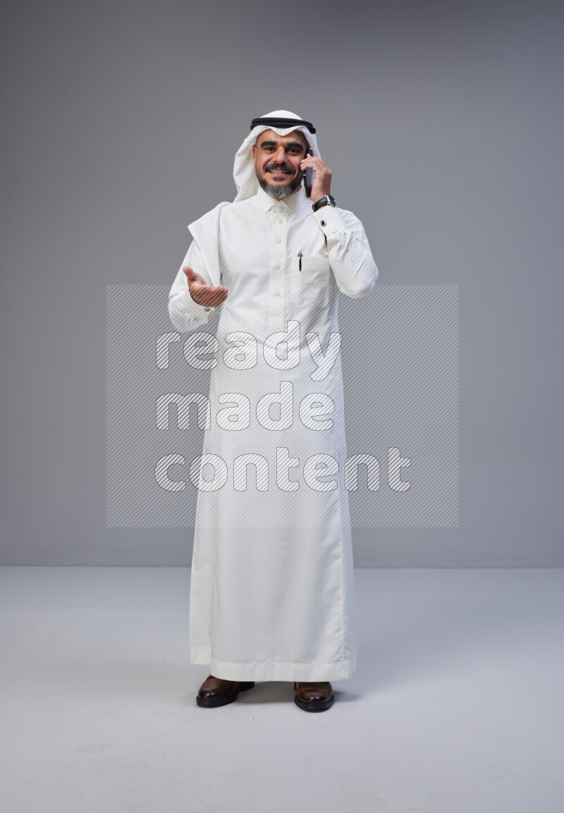 Saudi man Wearing Thob and white Shomag standing talking on phone on Gray background