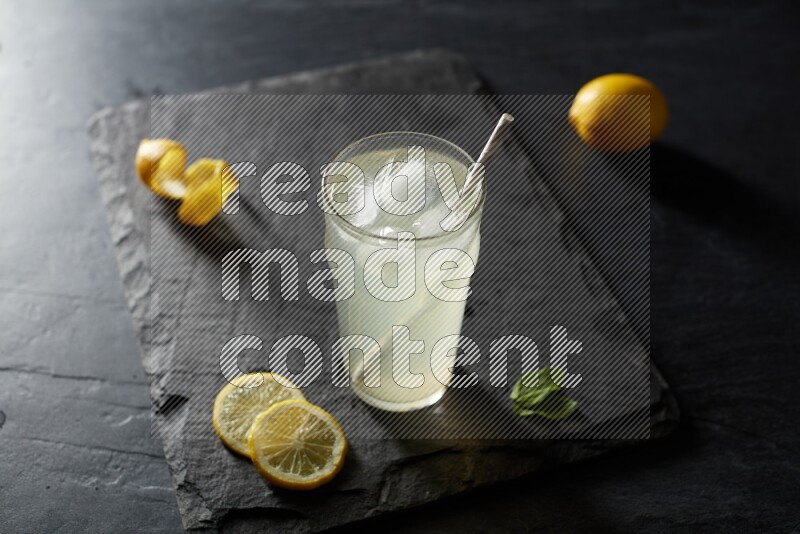 A glass of lemon juice with a straw on black background
