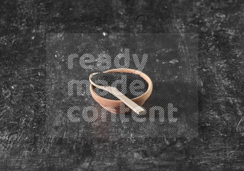 وعاء خشبي مع ملعقة خشبية ممتلئان ببذور حبة البركة علي خلفية سوداء