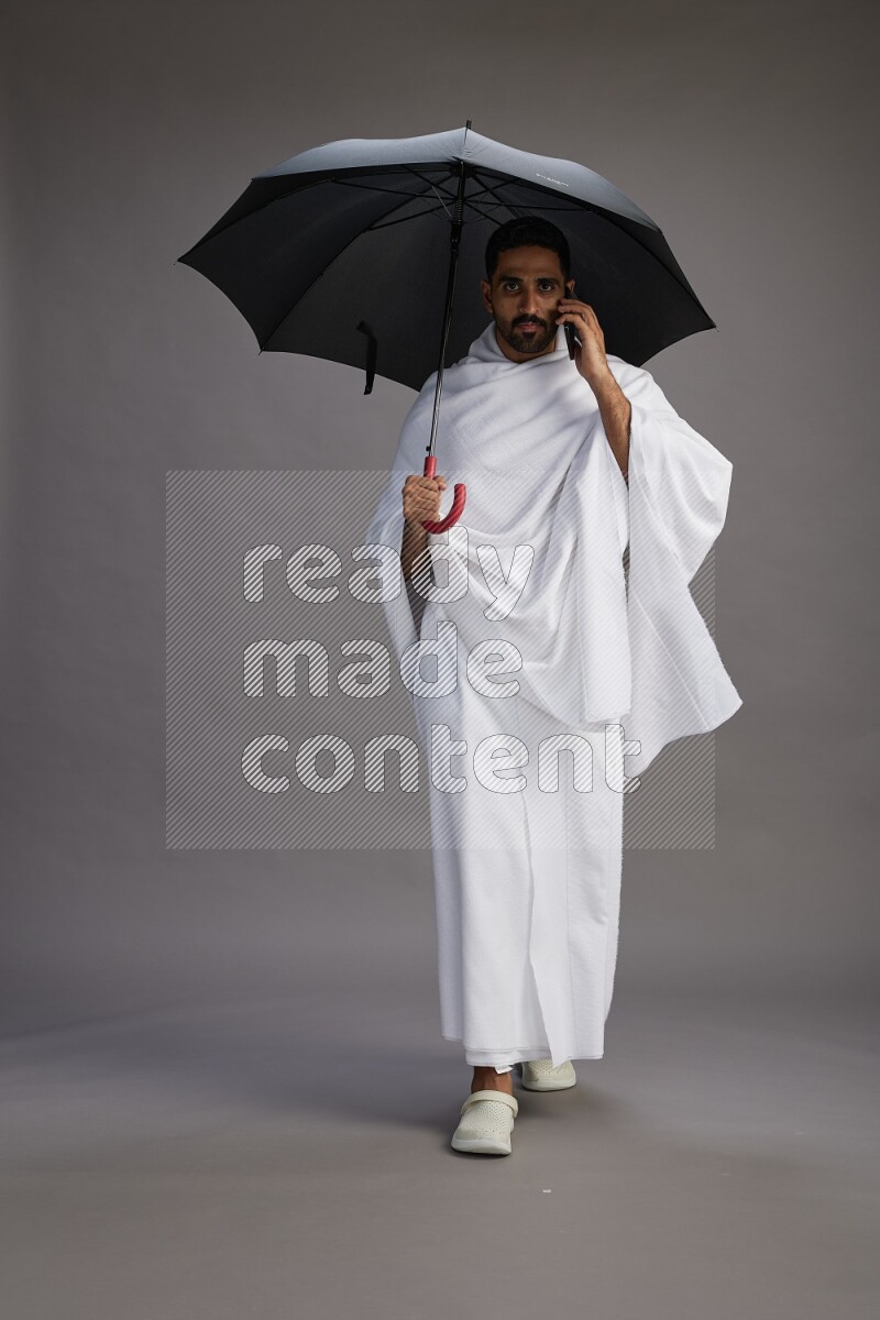 A man wearing Ehram Standing holding umbrella on gray background