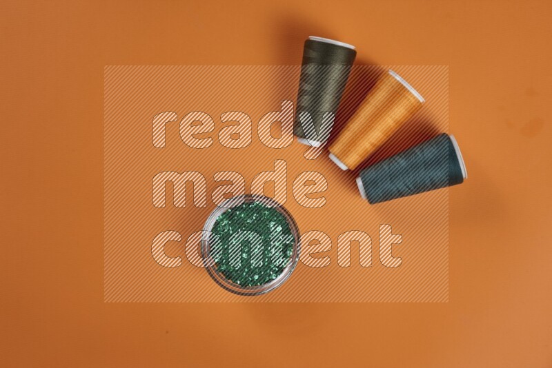 A green and orange collection of sewing and tailoring tools arranged on a orange background