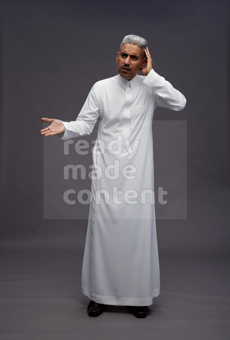 Saudi man wearing thob standing interacting with the camera on gray background