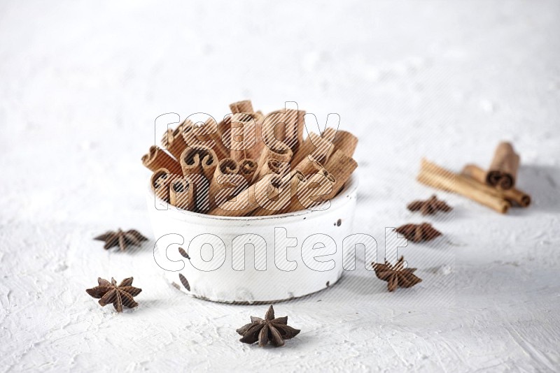 White bowl full of cinnamon sticks surrounded by star anis on a textured white background in different angles