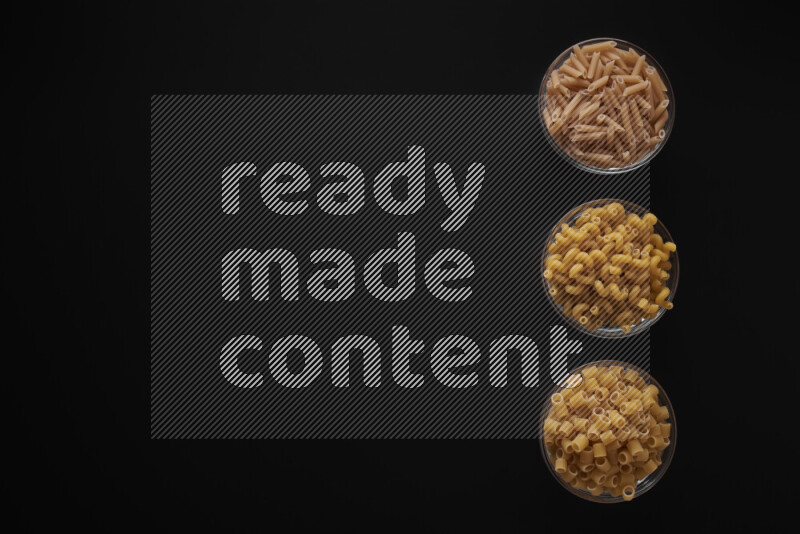 Different pasta types in 3 glass bowls on black background