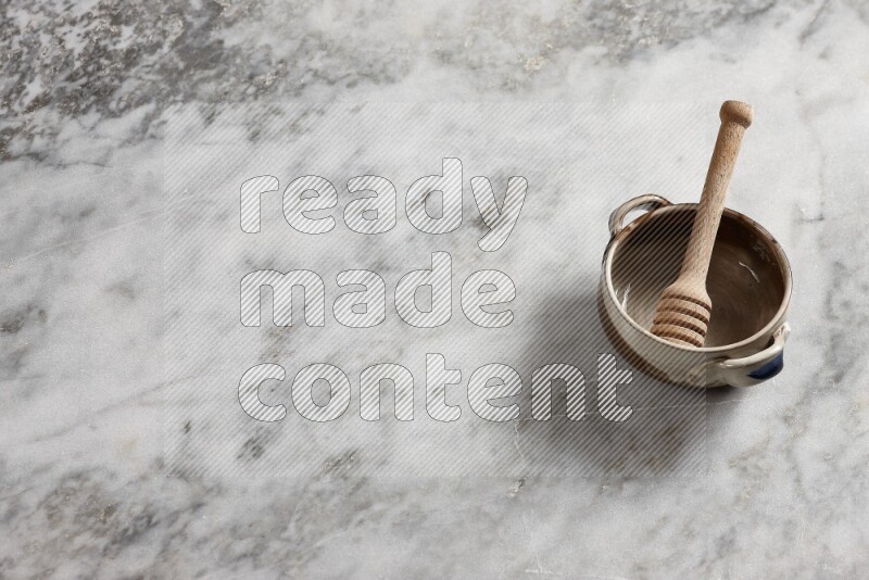 Multicolored pottery bowl with wooden honey dipper in it on grey marble background