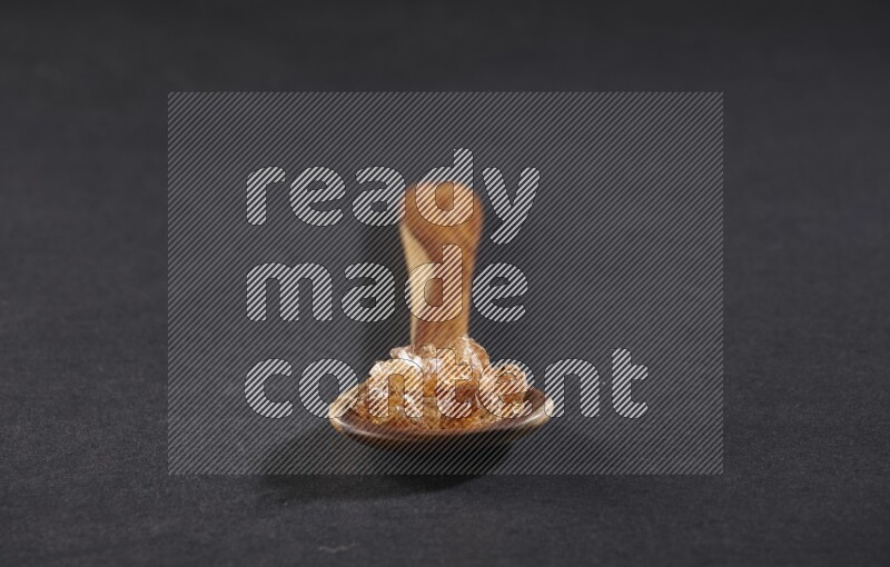 A wooden ladle filled with gum arabic on black flooring