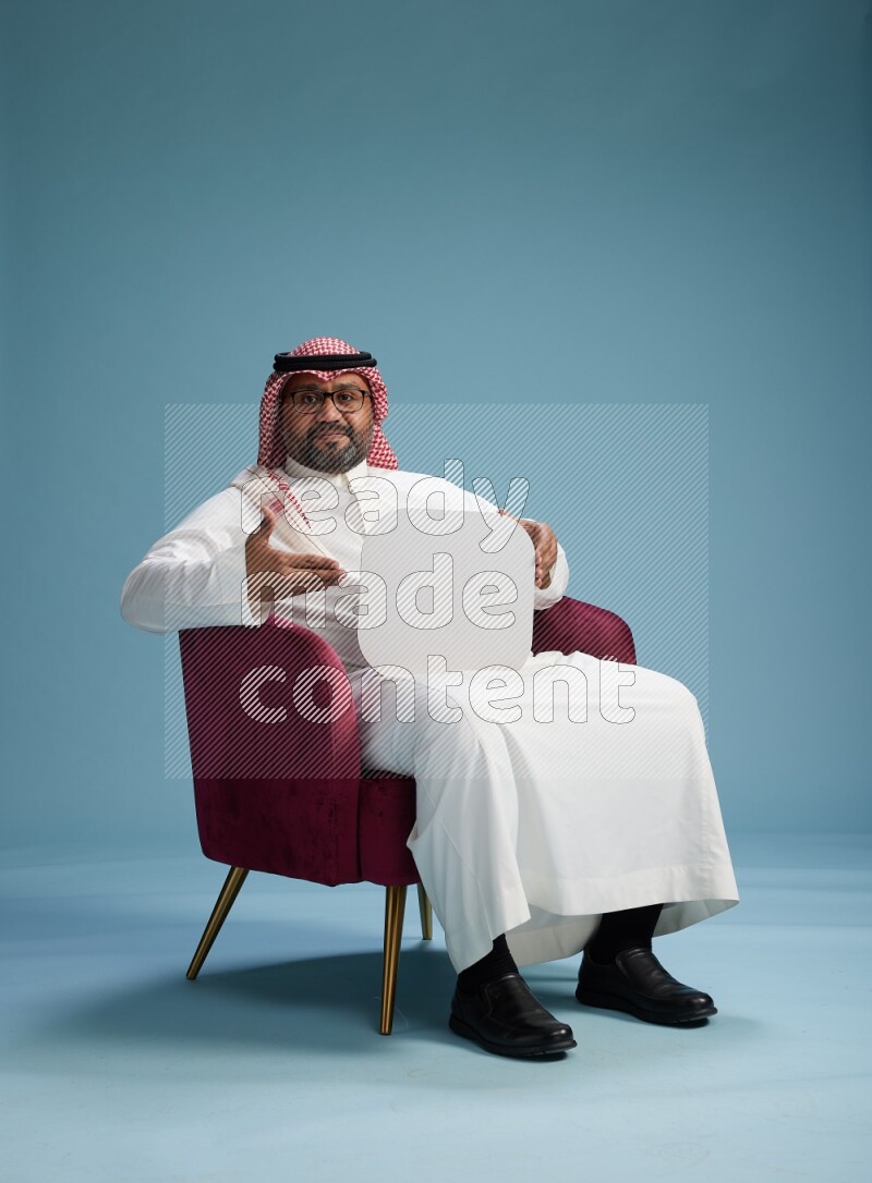 Saudi Man with shimag sitting on chair holding social media sign on blue background
